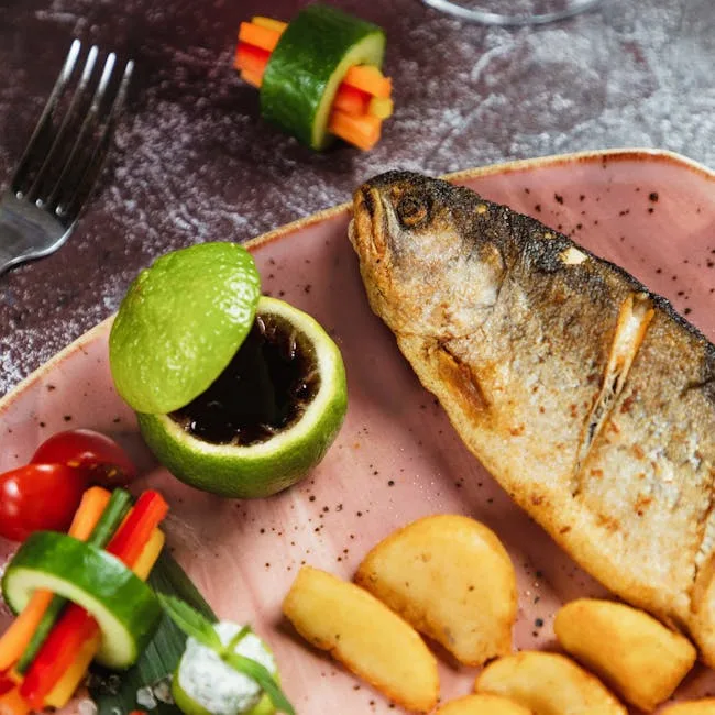 Ganzer gebratener Fisch mit Kartoffelspalten und Gemüsespießen auf Teller in Verona