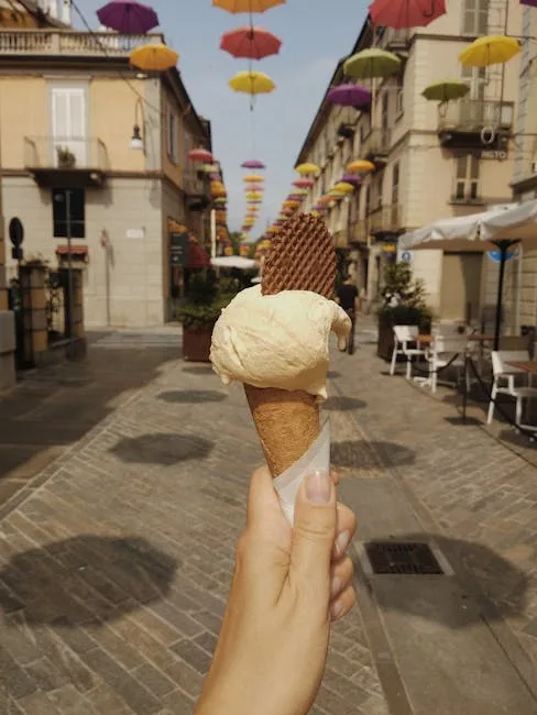 Hand hält Eiscreme vor einer mit Schirmen dekorierten Gasse in Verona
