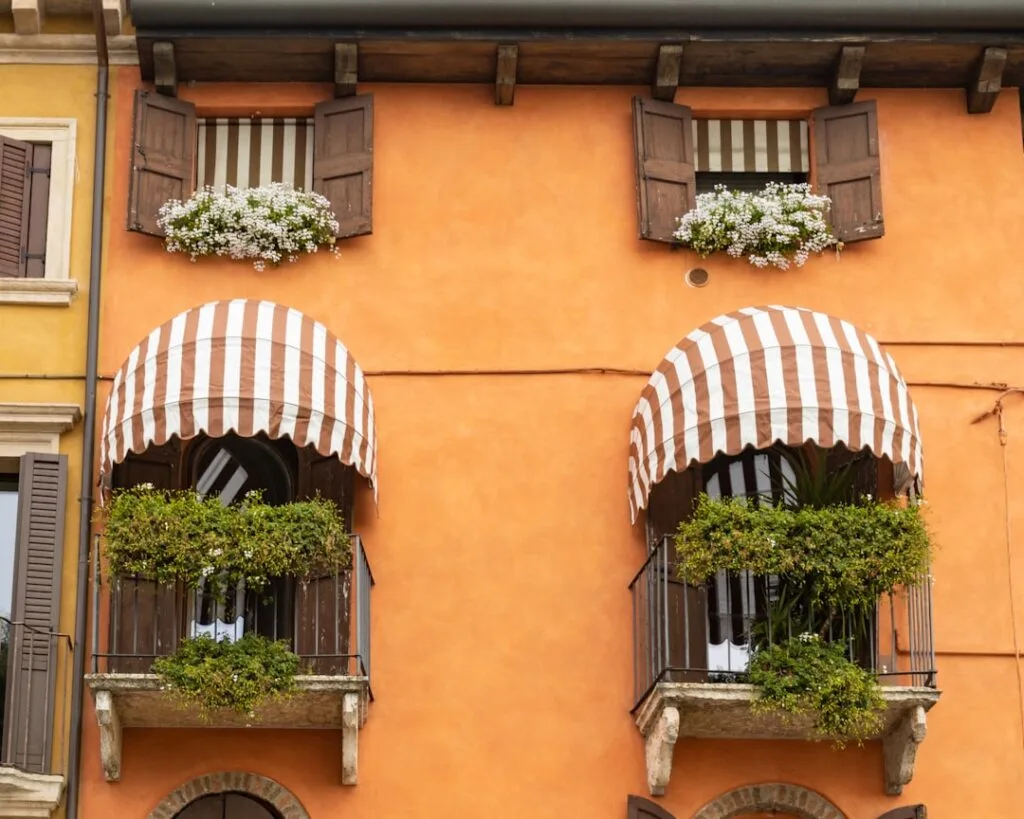Orange Fassade in Verona mit zwei Balkonen, gestreiften Markisen und Blumen