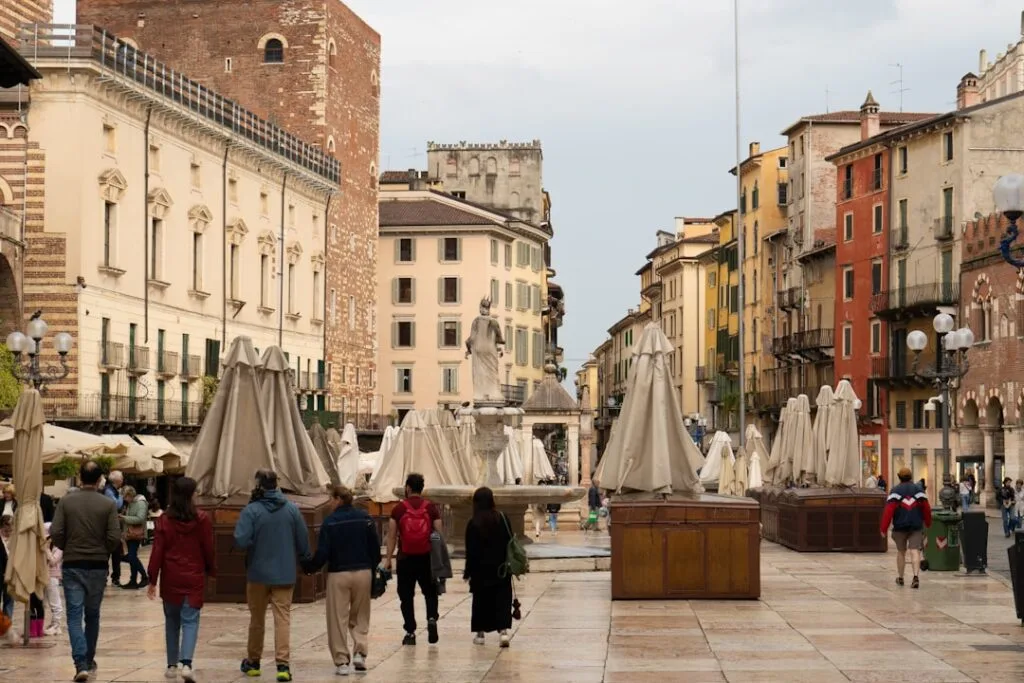 Menschen in Veronas Piazza mit zusammengeklappten Sonnenschirmen und Brunnen