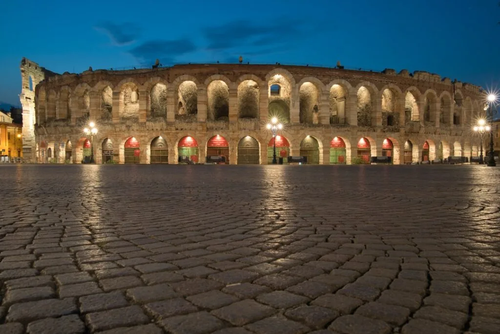 Façade éclairée de l'Arena de Vérone au crépuscule, pavés au premier plan