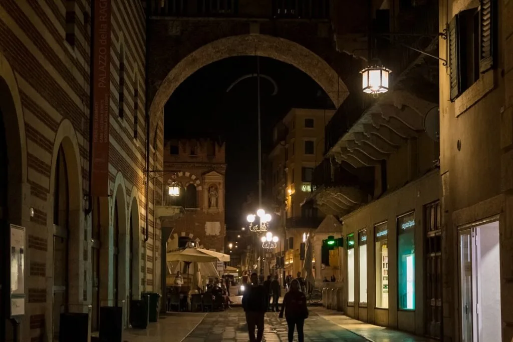 Rue piétonne nocturne à Vérone, arches et passants sous lanternes