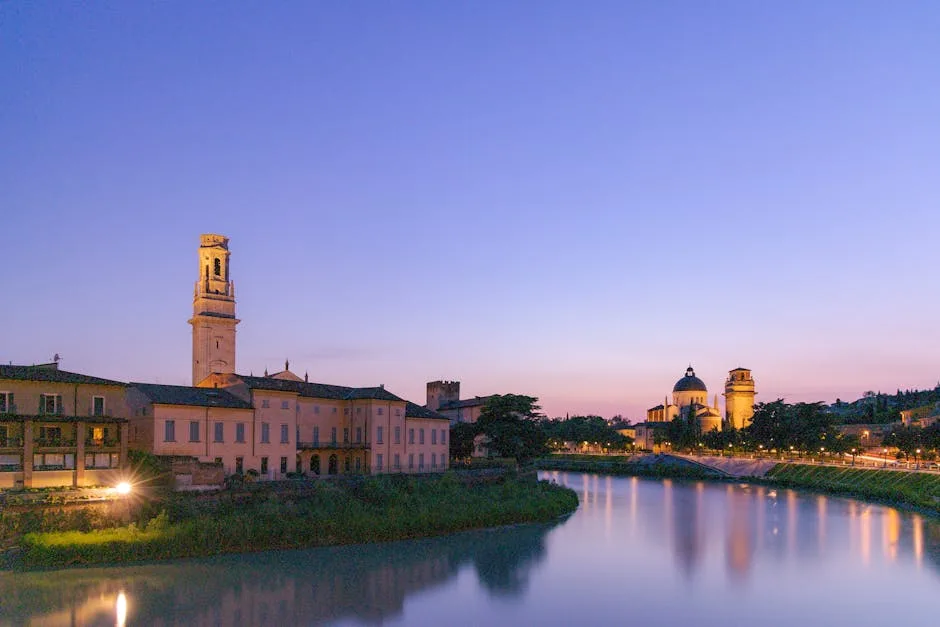 Ufer der Adige in Verona in der Dämmerung, beleuchtete Gebäude spiegeln sich im Wasser